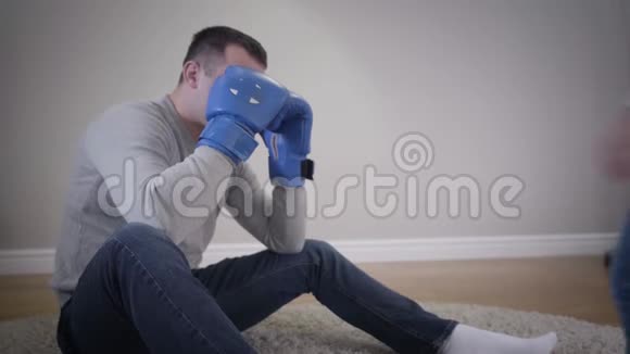 年轻开朗的白人男子在拳击手套后面隐藏着脸当他的小女儿上来拳击的时候视频的预览图