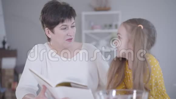 自信的成年女人在厨房和孙女交谈阅读食谱可爱的高加索小女孩视频的预览图