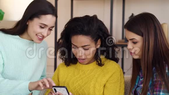 漂亮的多种族女孩坐在家里在智能手机上浏览互联网视频的预览图