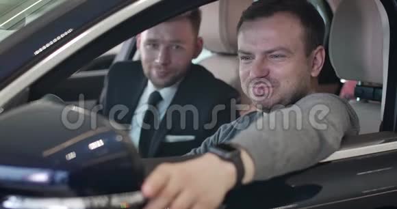 兴奋的白人年轻人坐在驾驶座上微笑肖像在车里听毒贩的成功男人视频的预览图