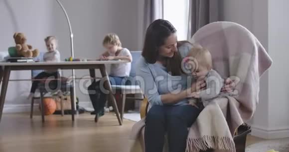 微笑的白种人女人爱抚小女孩摇着椅子妈妈很高兴在女儿的时候和宝宝玩视频的预览图