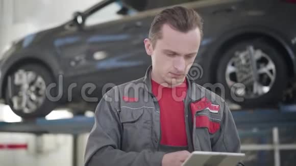 专业男性维修工程师的特写站在维修车间使用平板电脑高加索汽车修理工视频的预览图