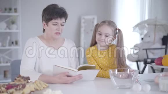 中年白种人妇女和小女孩的肖像为Shrovetide阅读美味煎饼的食谱祖母视频的预览图