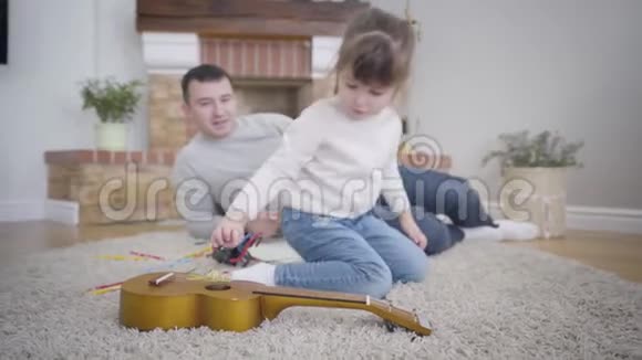 一位年轻漂亮的白种人女孩在后台和她微笑的父亲交谈时玩玩具视频的预览图