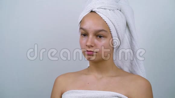 平静的女孩裹着浴巾坐在白色的工作室里视频的预览图