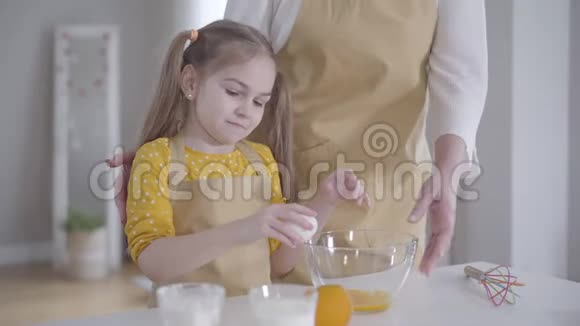 小白种人女孩把鸡蛋打碎成碗的肖像穿着围裙的快乐孩子帮助祖母视频的预览图