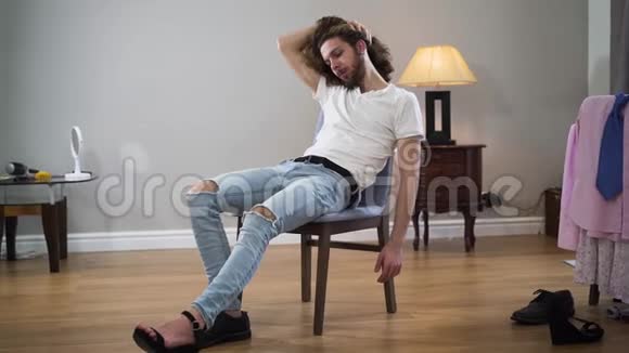 中镜头肖像年轻英俊的白种人男子坐在椅子上摸头发和看相机性别间视频的预览图