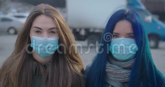两个戴着防护面具的年轻女人在繁忙的城市街道的背景下看着摄像机的特写脸肖像视频的预览图