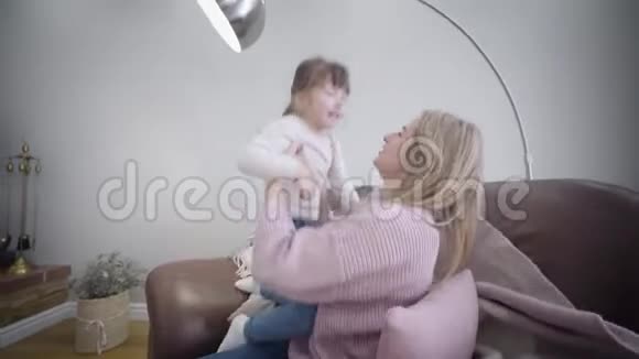 侧面看年轻的高加索美女坐在家里的扶手椅上和女儿玩快乐妈妈拥抱视频的预览图