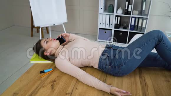 一个漂亮的女孩躺在办公室桌上打电话视频的预览图