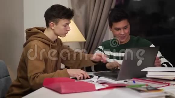 聪明的白人男孩帮助他的亚洲朋友处理笔记本电脑友好的多种族伙伴在室内学习视频的预览图