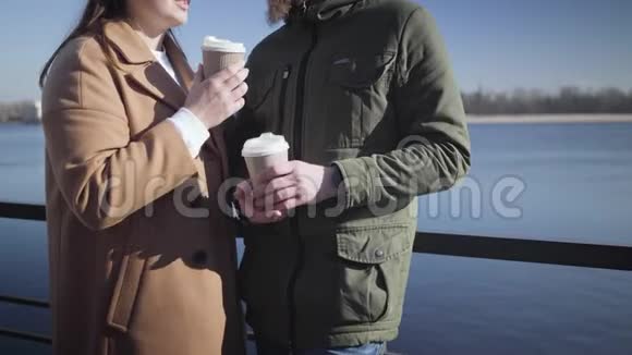 无法辨认的白人男孩和女孩在户外聊天和喝咖啡快乐的年轻夫妇在河岸上约会视频的预览图
