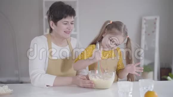 小美丽的女孩和祖母坐在厨房里用面粉打鸡蛋可爱的白种人小孩帮忙做饭视频的预览图