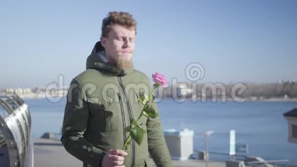 年轻的白种人红头发男子留着胡子和胡须等待心上人拿着玫瑰的肖像男朋友视频的预览图