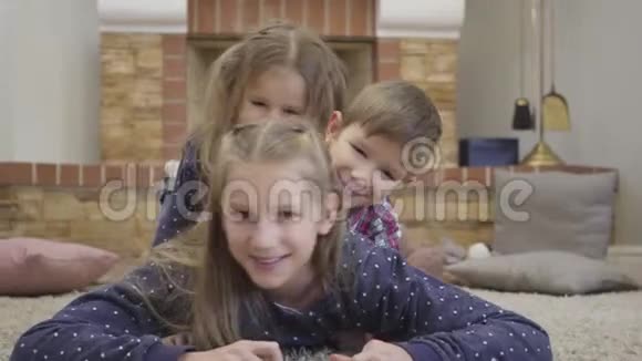 一个笑容满面的白人女孩躺在地板上年幼的孩子在她身上涂鸦令人愉快的兄弟姐妹视频的预览图
