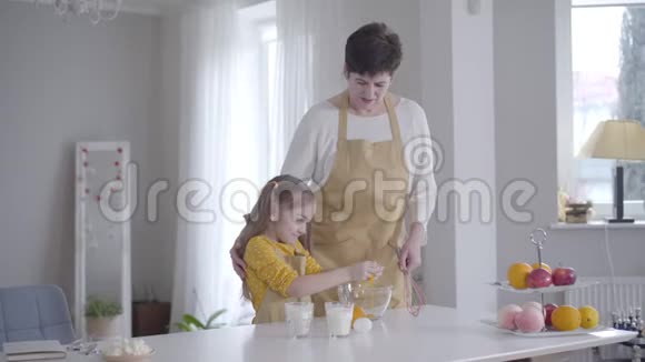 小可爱的白种人女孩把鸡蛋打碎成碗微笑着孙女高兴帮奶奶做煎饼视频的预览图
