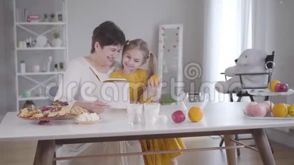 微笑的白人女人拥抱孙女帮助她做饭小可爱的女孩拿着橘子微笑着视频的预览图
