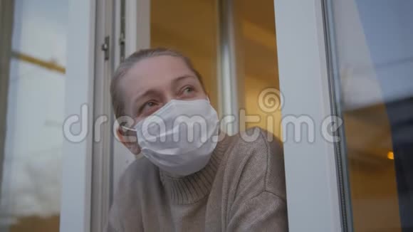一个戴着医用口罩的妇女从窗口向外看摘下了口罩视频的预览图