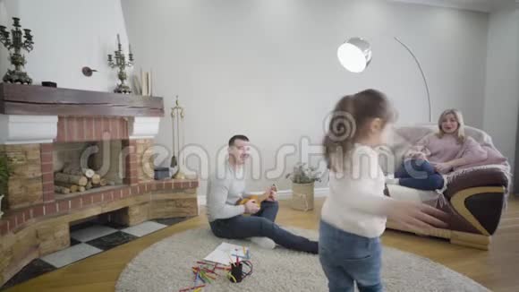 一个活泼的白人黑发女孩的画像她的父亲在玩四弦琴母亲坐在沙发上视频的预览图