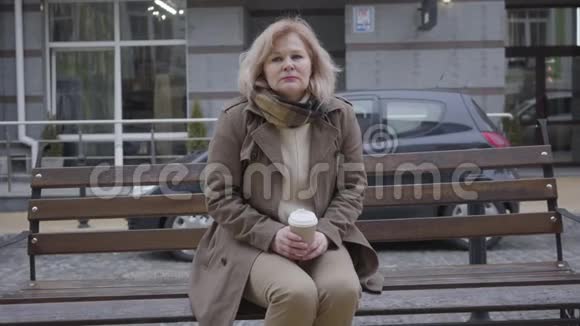 美丽的中年白种人妇女在城市街道上喝咖啡和思考的肖像高级有思想的退休人员视频的预览图