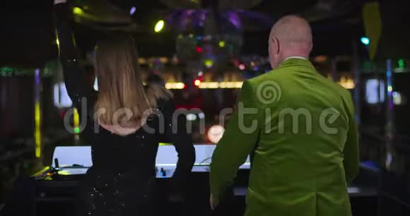 年轻迷人的白种人女人和年长快乐的男人在夜总会舞台上跳舞女性DJ视频的预览图