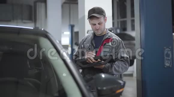 白种人严重维修工程师用数字设备检查汽车的肖像穿工作服的成年男子视频的预览图