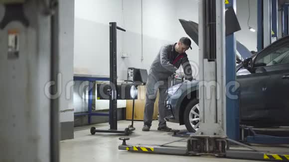 汽车维修车间内的大型专业汽车机械调整防雷设备白种人男人拧螺丝视频的预览图