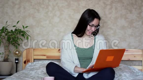 年轻漂亮的女孩正在用她的笔记本电脑工作坐在家里的床上年轻可爱的女孩正坐在床上打字视频的预览图