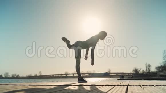 年轻的运动女孩有很大的伸展是在美丽的日落和湖的背景上的分裂慢动作视频的预览图