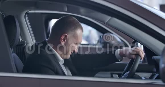 微笑白人男子触摸方向盘和环顾汽车内部成功的年轻商人视频的预览图