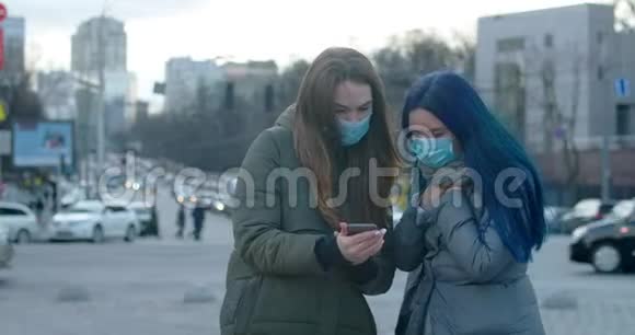使用智能手机戴防护面具的年轻女性布鲁内特女孩一边走一边她的朋友咳嗽Covid19号承运人视频的预览图