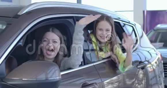 积极的白人母亲和女儿挥手从新优雅的黑色汽车在经销商微笑快乐的女人和小女孩视频的预览图