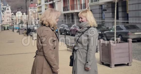 在阳光明媚的秋日两位开朗的高级女性在城市街道上交谈领取养恤金的白种人正退休视频的预览图
