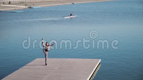 年轻的运动女孩伸展很大是码头上的裂口对湖的蓝色视频的预览图