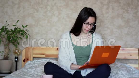 年轻迷人的女孩在家坐在床上远程工作视频的预览图