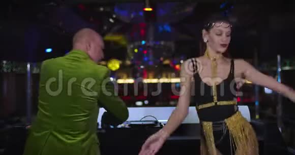 回到活跃的老白种人DJ混合音乐使用控制器作为年轻的围棋舞者穿着诱人的裙子跳舞视频的预览图