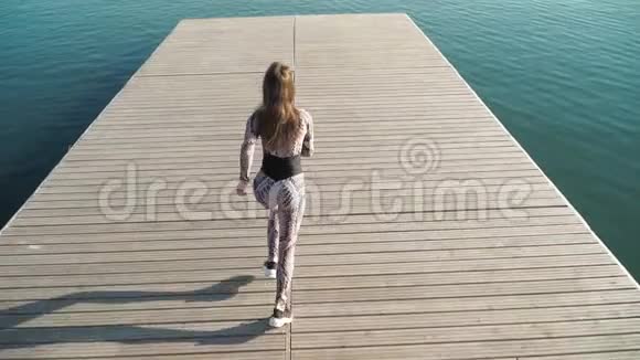 一位身材优美的女运动员在湖边的码头上奔跑慢动作顶部视图视频的预览图