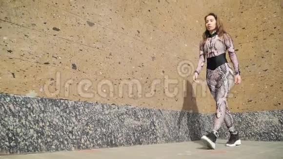 穿着运动服的漂亮年轻运动女孩优雅地沿着棕色的混凝土墙走慢动作对斯泰迪达姆的射击视频的预览图
