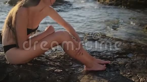女人正在腿上涂防晒霜坐在海边视频的预览图