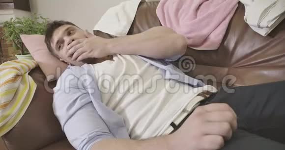 一个懒散的年轻白种人的特写他打着哈欠躺在家里的扶手椅上疲惫的帅哥在家休息视频的预览图