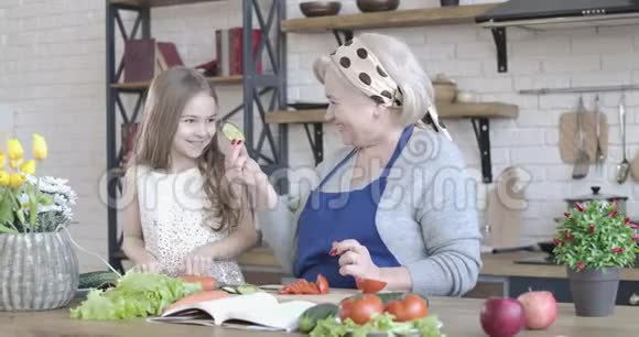 积极高加索祖母和孙女在厨房品尝切黄瓜的肖像可爱的小女孩视频的预览图