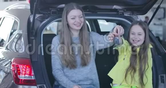 年轻的白种人女人和小可爱的女孩坐在后备箱里吹嘘钥匙积极的母女购买视频的预览图