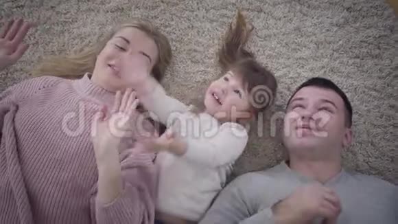乐观的白人父亲母亲和小女儿躺在地毯上捕捉肥皂泡微笑视频的预览图