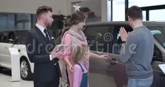 年轻的高加索家庭在汽车陈列室挑选新汽车男人女人还有小可爱的女孩视频的预览图