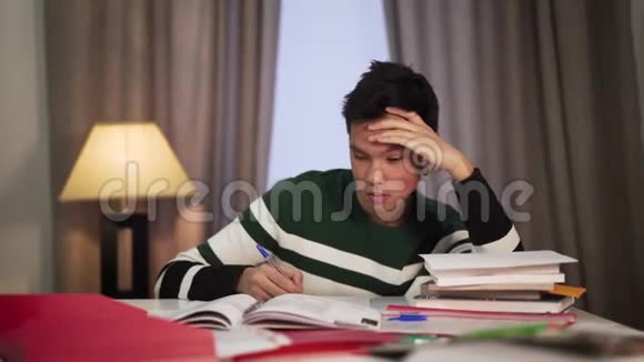 精疲力竭的亚洲男孩在室内做作业时睡着了聪明英俊的学生过度工作教育视频的预览图