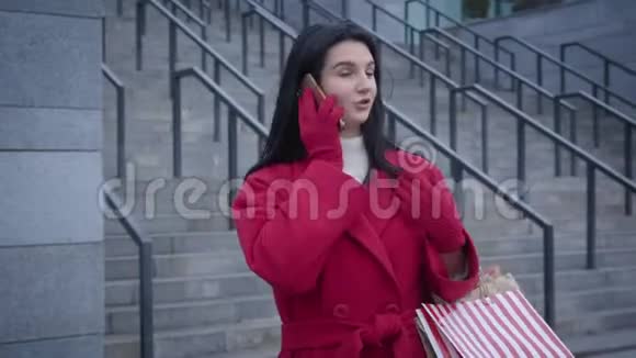 年轻开朗的白人女孩在电话里说话微笑着站在城市街道上快乐的红色女人视频的预览图