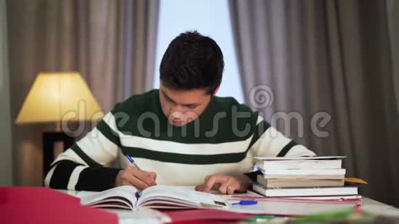疲惫的亚洲男大学生坐在家里看书的肖像年轻英俊的男孩把头放在手上视频的预览图