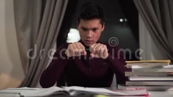 愤怒的亚洲男孩打破铅笔坐在桌子旁的肖像晚上在室内学习的脾气暴躁的男孩视频的预览图