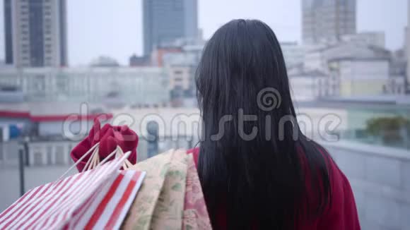后景的时尚女士黑发站着购物袋转向相机和眨眼优雅的女人视频的预览图