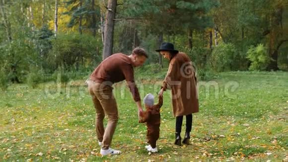 小儿子牵着爸爸和妈妈的手幸福的一家人在秋天公园散步视频的预览图
